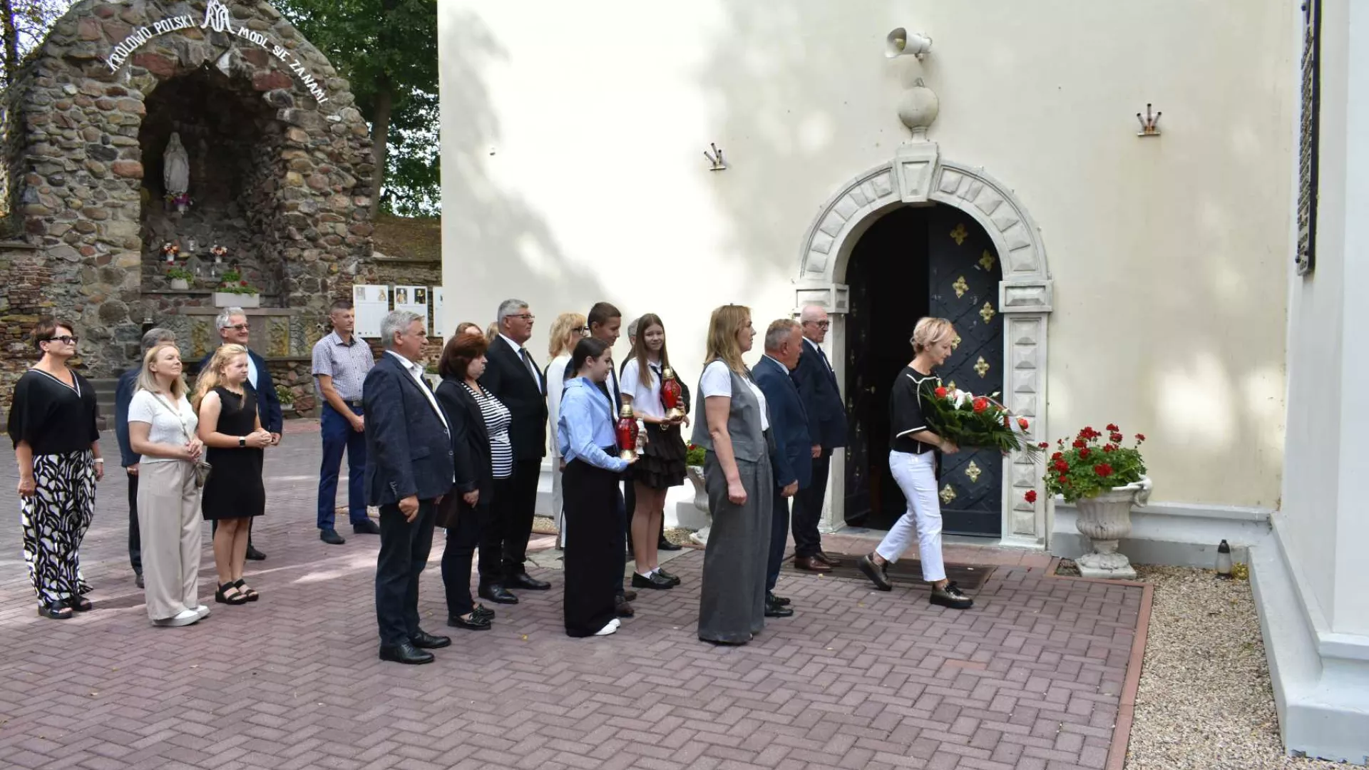 Złożenie kwiatów pod tablicą pamiątkową na ścianie kościoła w Dankowie.