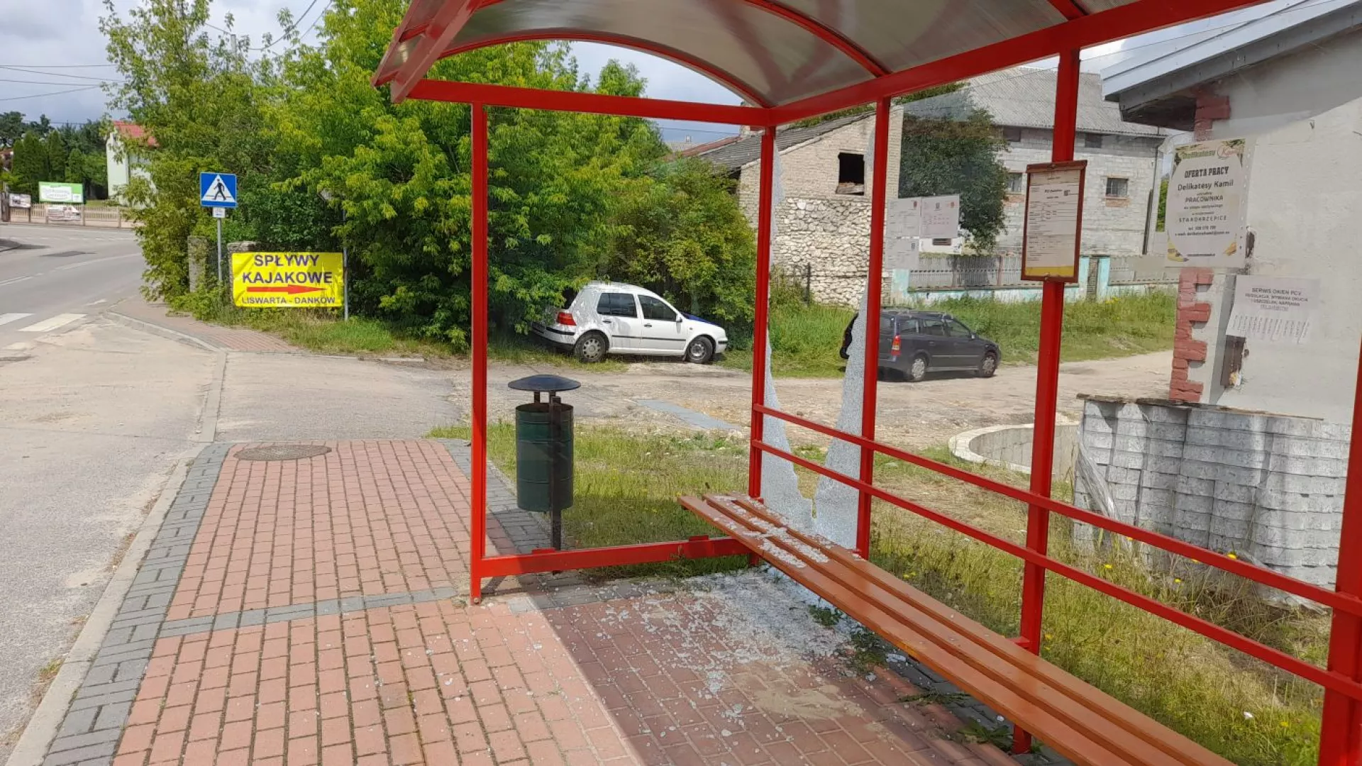 Na zdjęciu wiata przystankowa w Dankowie ze stłuczoną szybą, wokół okruchy szkła, w tle droga i domy w Dankowie