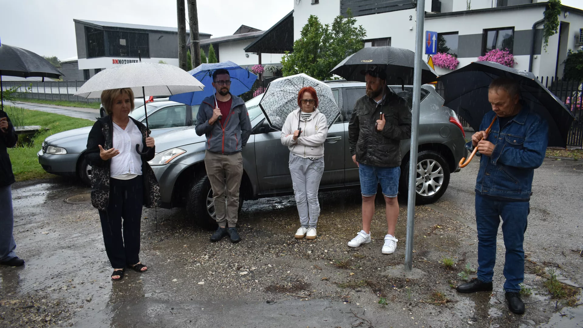 Spotkanie z przedstawicielami GDDKiA w Parzymiechach. Na zdjęciu m.in. Wójt Gminy Lipie, radni z Parzymiech i mieszkańcy. Głos zabiera wójt. Wszystkie osoby trzymają otwarte parasole.