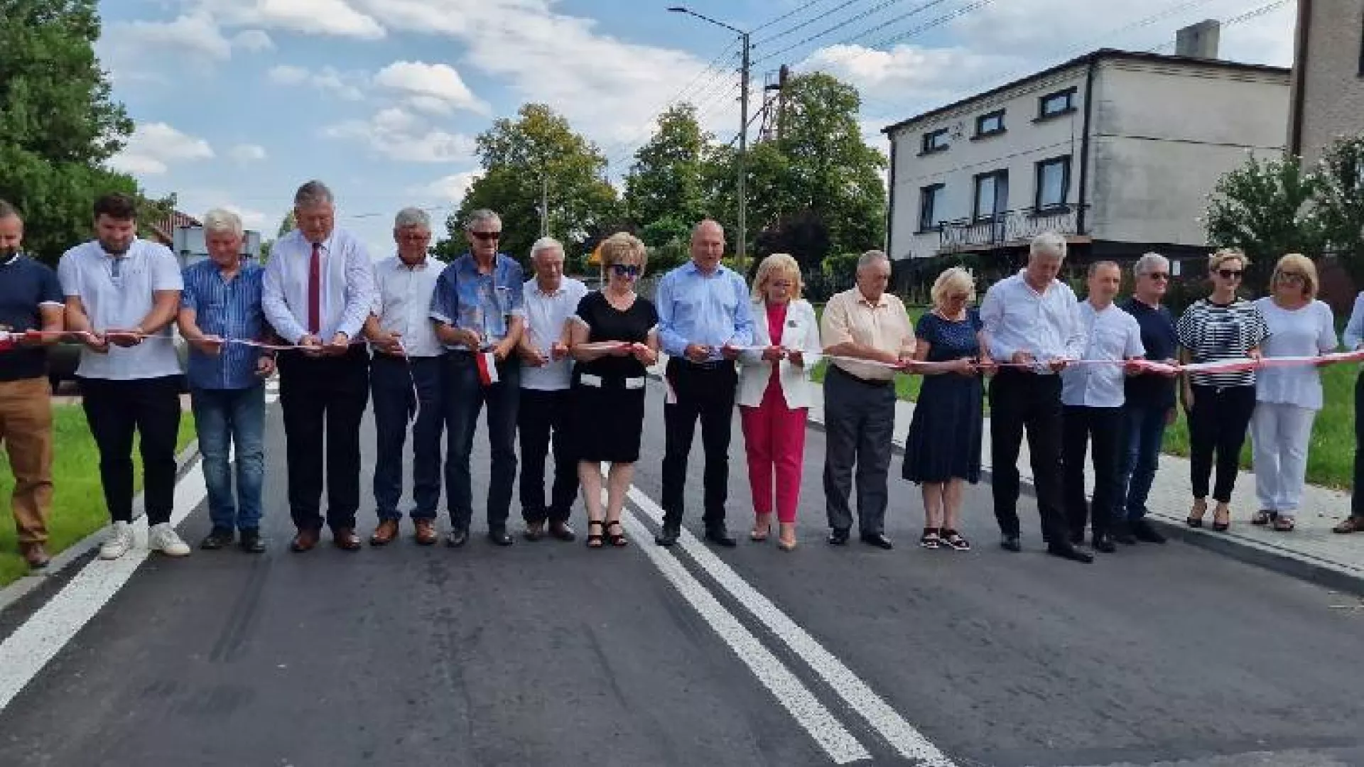 Uczestnicy uroczystego otwarcia drogi dokonują przecięcia wstęgi.