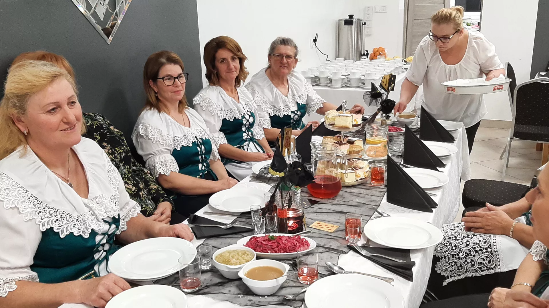 Uczestnicy biesiady andrzejkowej siedzą za stołem zastawionym talerzami z tradycyjnymi potrawami regionu.