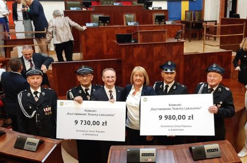 Przedstawiciele OSP Albertów i OSP Zimnowoda oraz wiceprzewodnicząca Rady Gminy Lipie Alicja Podgórska wraz z członkiem Zarządu Województwa Śląskiego Grzegorzem Boskim trzymają symboliczne czeki z kwotami przyznanych dotacji.