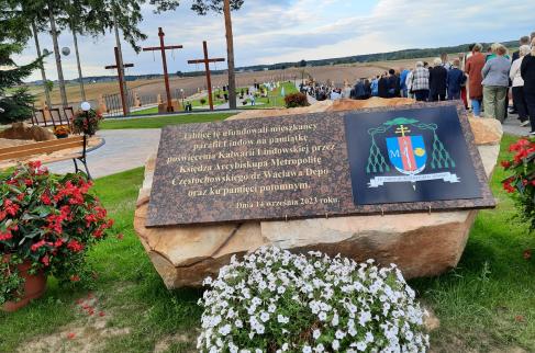 Tablica pamiątkowa z okazji poświęcenia Kalwarii Lindowskiej. W tle – tłum uczestników uroczystości podczas modlitw na terenie kalwarii.