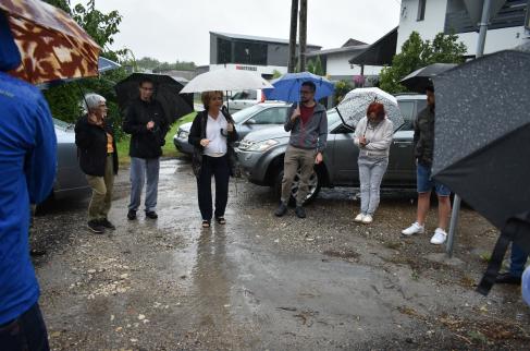 Spotkanie z przedstawicielami GDDKiA w Parzymiechach przy skrzyżowaniu drogi krajowej z ulicą Starowiejską. Na zdjęciu m.in. Wójt Gminy Lipie, radni z Parzymiech i mieszkańcy. Z powodu deszczu większość osób trzyma otwarte parasole. W tle widoczne zaparkowane samochody.